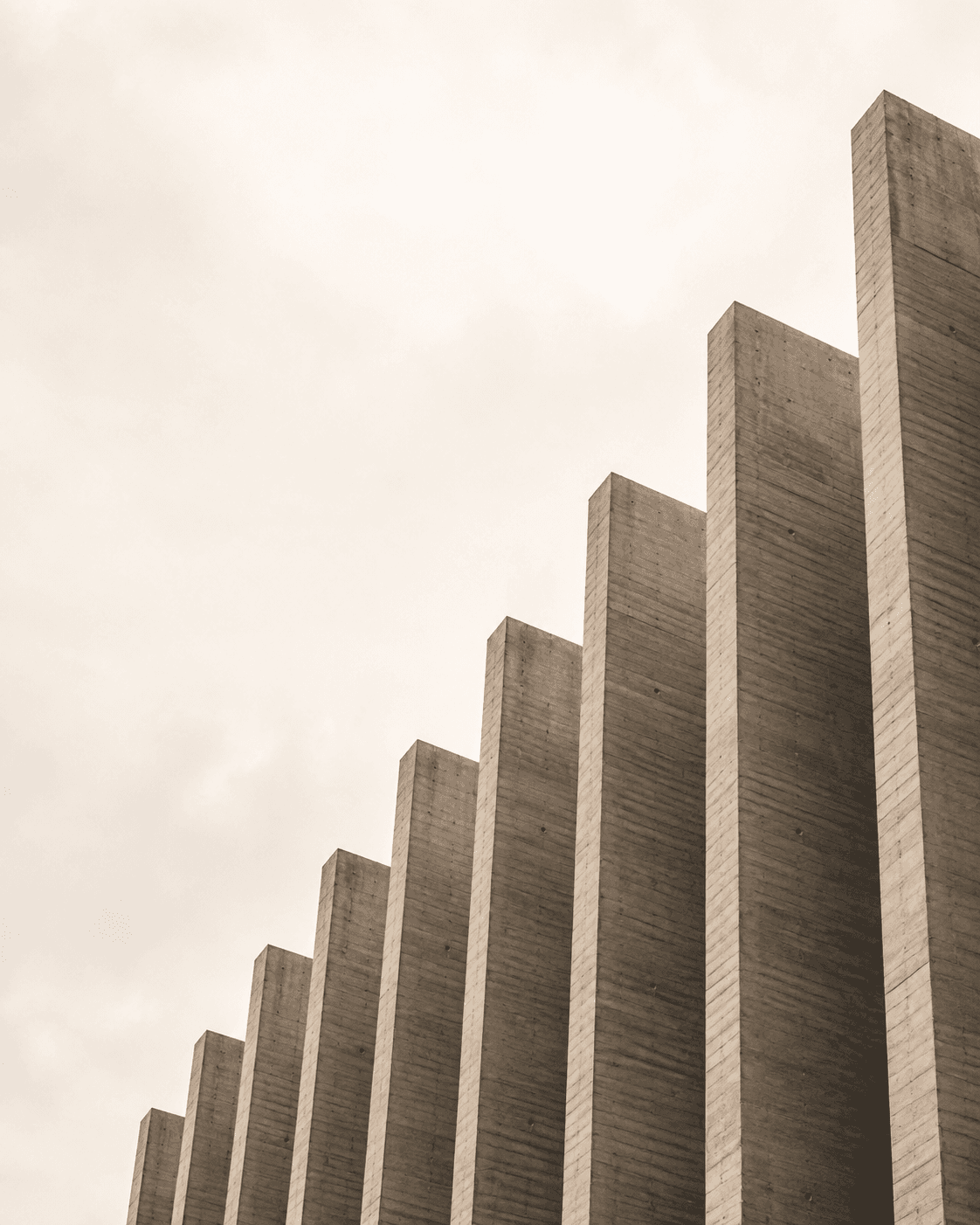 Looking up at a concrete facade of tall vertical fins of varying height against a pale sky.