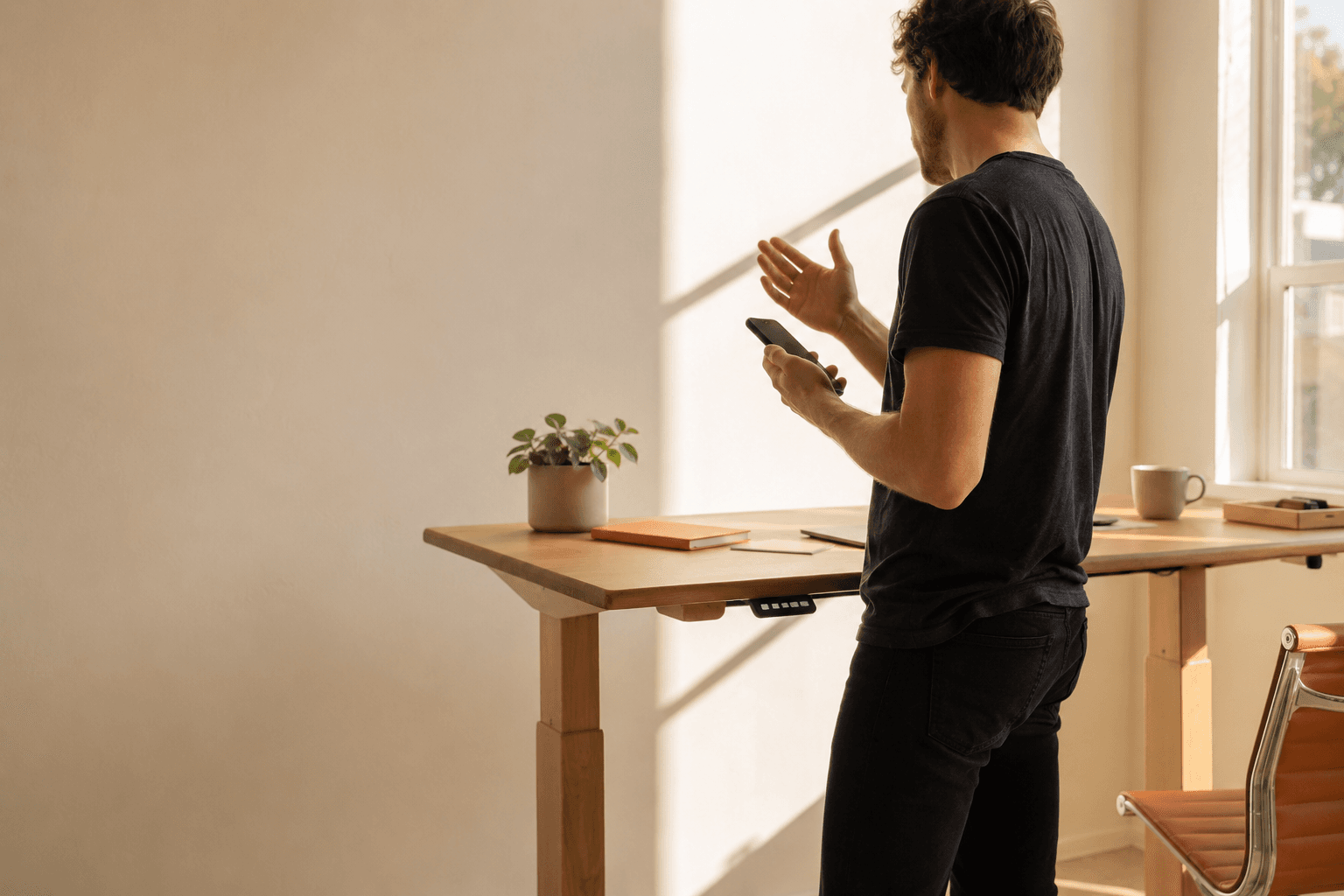 A person at a standing desk mid-conversation, phone in hand, one hand raised in explanation.